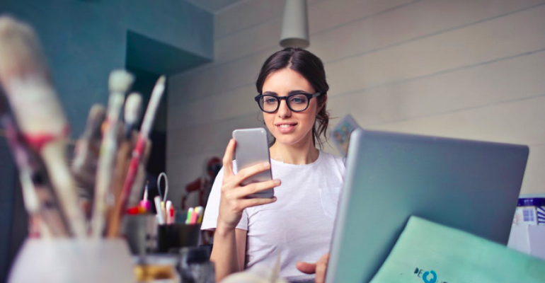 Woman holding smartphone at computer.png